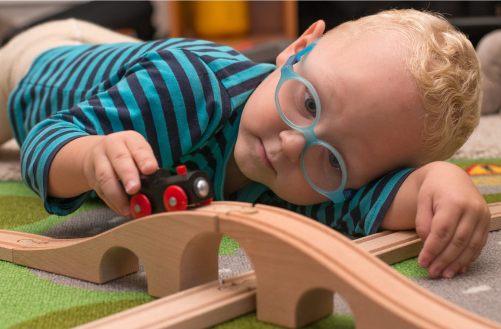 Child with glasses laying down on ground to play with his train toy set.