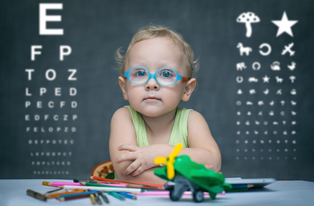 Child sitting at table with her glasses on and eye exam readings in the background.