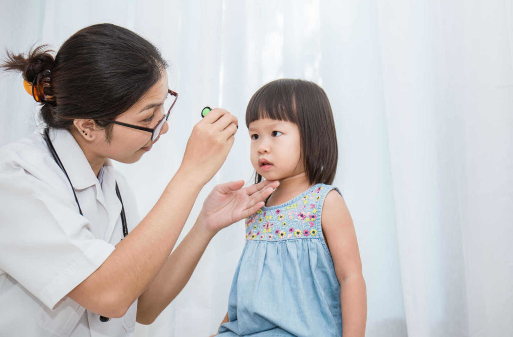 A female doctor with a flashlight in her right hand is examining the eye of a toddler.