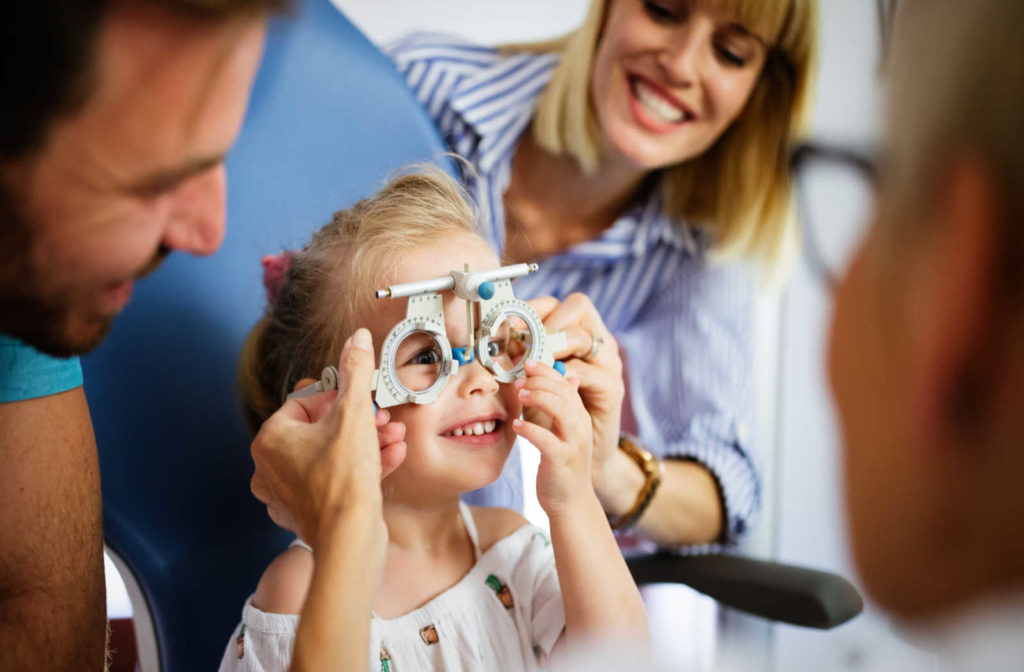 A young girl getting her eyes tested by an optometrist with her parents by her side smiling