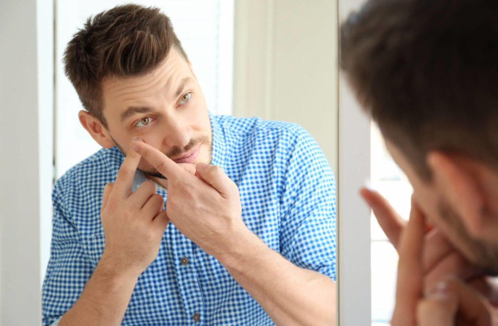 A man looking into a mirror while he uses his right hand to put a contact lens in his left eye.