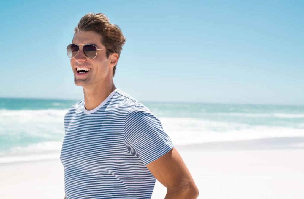 A man in casual clothing wearing sunglasses and smiling at the beach.