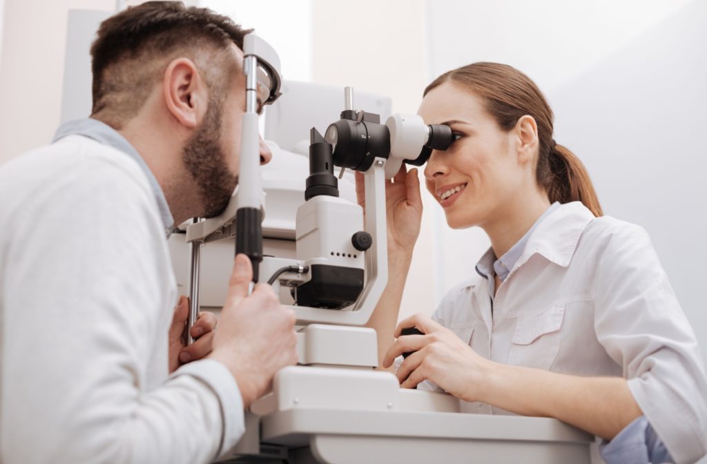 A smiling female ophthalmologist carefully examining a male patient's eyes to diagnose sinusitis.