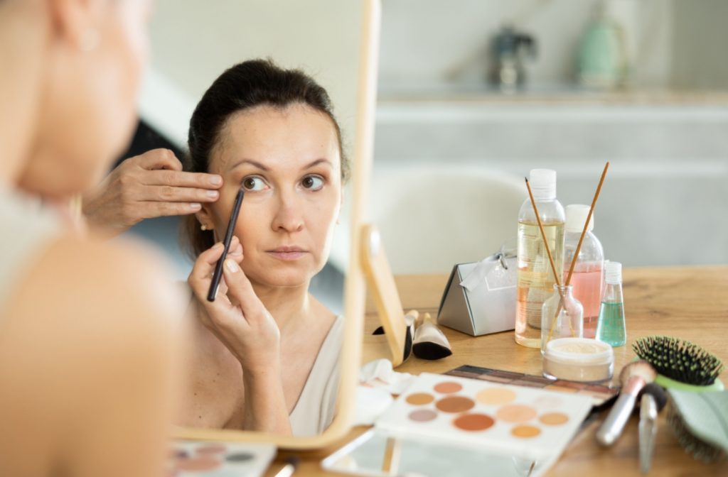 A closeup of a woman applying her eye makeup while focusing on the mirror.