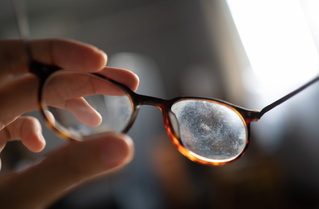 Close-up of scratched eyeglass lenses held by a hand, showing visible lens damage.