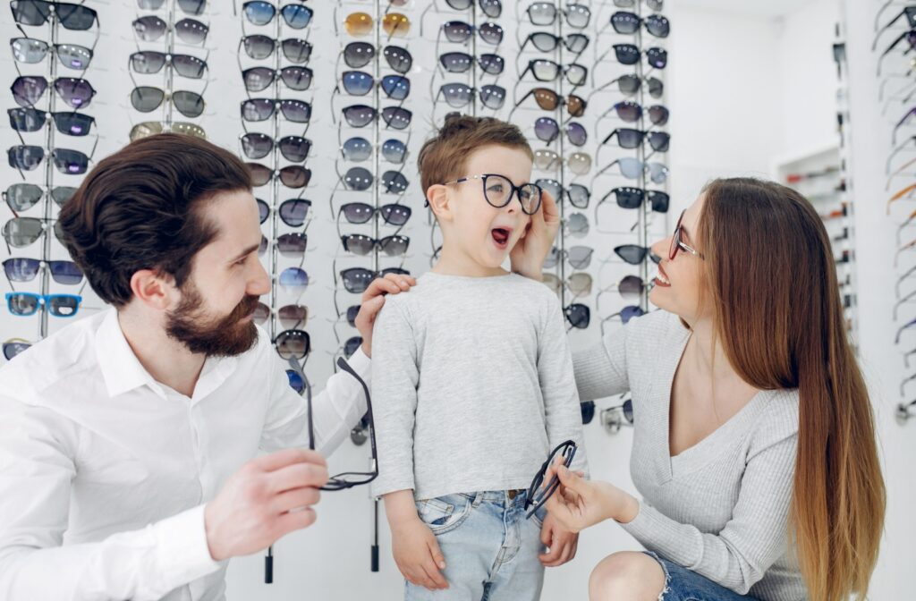 A family in front of an optical display at an optometry office, trying on different frames.