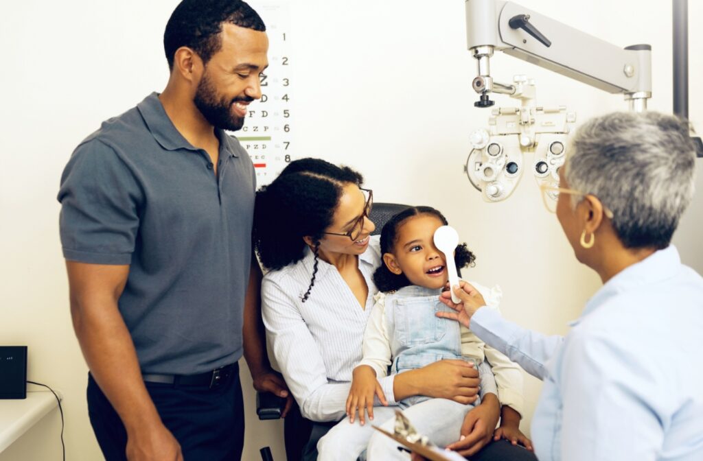A family in an eye exam room, having their child's eye's assessed by an eye doctor.