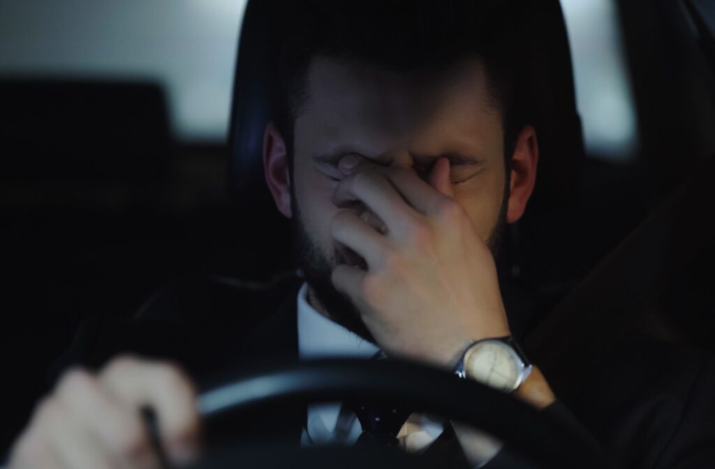 A person rubbing their eyes while driving, due to changes in night vision.