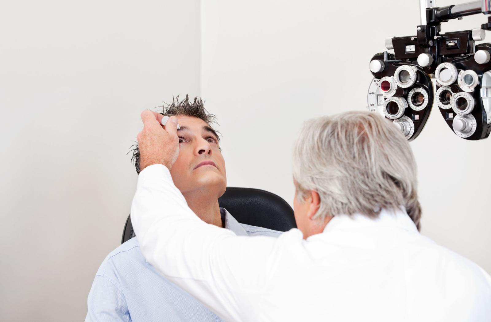 An eye doctor inserting eye drops into a patient's eye.